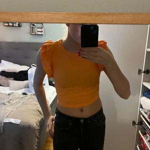 Orange ribbad topp från Zara - Säljer en snygg orange ribbad topp från Zara med volangdetaljer på axlarna. Toppen är croppad och ärmlös, perfekt för sommardagar. Passar utmärkt till både jeans och kjol. 🌟