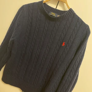 Mörkblå stickad tröja från Polo Ralph Lauren - Säljer en snygg mörkblå stickad tröja från Polo Ralph Lauren med kabelstickat mönster och röd broderad logga på bröstet. Väldigt bra på att hålla värme vilket är extra skönt nu under kalla vintern. Skriv gärna om du har några frågor! OBS! Är utomlands mellan 21 dec - 4 jan, så kan skicka om beställningen sker senast 20:e, efter det tidigast 5 jan.