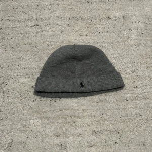 Polo Ralph Lauren mössa - Snygg grå mössa från Polo Ralph Lauren med broderad logga. Perfekt för kyliga dagar och ger en stilren look. Tillverkad i mjukt material för extra komfort.