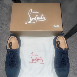 Mörkblå sneakers från Louboutin - Snygga mörkblå sneakers från Louboutin med klassisk röd sula. Skorna har snörning och är tillverkade i mocka med en stilren design. Perfekta för en trendig look.