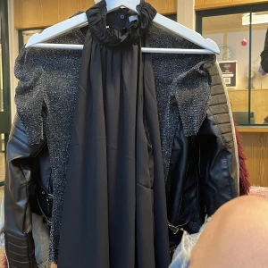 Svart topp - Elegant svart tröja med hög krage. Toppen har en lös passform och är ärmlös, vilket ger en stilren look. Perfekt för festliga tillfällen.