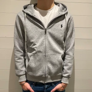 Ralph lauren hoodie - Säljer en stilren grå hoodie från Polo Ralph Lauren med dragkedja och klassisk logga på bröstet. Perfekt för en avslappnad look. Den är i storlek M och modellen är 180cm lång. Den är i princip nyskick och originalpåse medföljer! Vid övriga funderingar eller frågor är det bara att höra av sig🙌 priset går alltid att diskuteras!