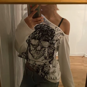 Vit offshoulder tröja med döskalletryck från Romwe - Säljer en cool vit offshoulder tröja från Romwe med ett stort svart döskalletryck på framsidan. Tröjan har långa ärmar och en avslappnad passform. Perfekt för en drainer stil. 💕