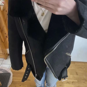 Svart jacka från Zara - Snygg svart jacka från Zara med dragkedja och bälte i midjan. Har en mjuk, pälsliknande insida för extra värme. Köpt för 1500kr och är i princip i nyskick. Perfekt för kyligare dagar💓🙌🏼