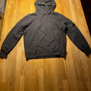 Svart hoodie från C.P. Company - Säljer en svart hoodie från C.P. Company. Tröjan har en praktisk magficka och en justerbar huva med dragsko. Tröjan är i Xs.| Skick 7/10.                            Fler frågor och bilder i chatten om du är intresserad.
