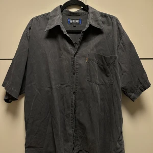 Svart kortärmad skjorta från Jack & Jones - Snygg svart kortärmad skjorta från Jack & Jones med klassisk krage och knappstängning. Perfekt för en avslappnad och boxy stil. Skjortan har en bröstficka för extra detalj.