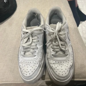 Vita Nike Air Force sneakers - Säljer ett par klassiska vita Nike Air Force sneakers med snörning. Skorna har en perforerad tå och en robust sula för extra komfort. Perfekta för en stilren look.