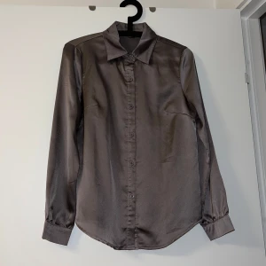 Grå skjorta från Shein - Elegant grå skjorta från Shein i satinmaterial. Skjortan har långa ärmar och knappar framtill, perfekt för en stilren look.