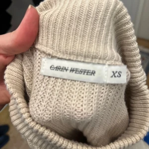 Beige stickad tröja från Carin Wester - Säljer en stilren beige stickad tröja från Carin Wester i storlek XS. Tröjan har en ribbad design med långa ärmar och en hög hals. Perfekt för kyligare dagar!