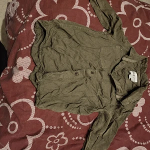 Olivgrön henley-skjorta - Säljer en olivgrön henley-skjorta från H&M. Skjortan har långa ärmar och knappar framtill. Perfekt för en avslappnad stil. Fin att ha till festligt tillfälle :)