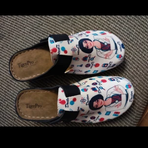 Färgglada tofflor från TigerPro - Säljer ett par unika och färgglada tofflor från TigerPro. De har ett roligt mönster med tecknade figurer och symboler i olika färger. Perfekta för att liva upp vardagen hemma! Tofflorna är bekväma och lätta att ta på. Ortopedisk skor passar i vården 