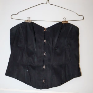 Svart korsett från H&M - Snygg svart korsett från H&M i storlek S. Den har en klassisk design med hyskknäppning framtill. Perfekt för en festlig kväll eller som en stilren detalj under en kavaj. Materialet känns slitstarkt och bekvämt.