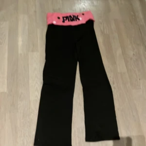Svarta byxor med rosa midja  - Säljer ett par svarta byxor med en cool rosa midja. De har en loose passform och är perfekta för en avslappnad stil. Midjan har ett prickigt mönster och texten 'PINK' i svart. Superbekväma och stiliga för vardagsbruk!