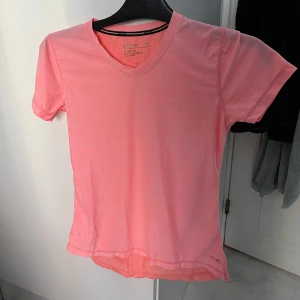 Rosa träningstopp från SOC - Säljer en rosa träningstopp från SOC i storlek XS. Den har en v-ringad hals och korta ärmar, perfekt för träning. Materialet är lätt och andas bra, med en reflekterande detalj på ryggen för extra synlighet. Toppen är i mycket bra skick. 