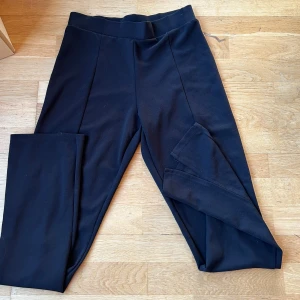 Svarta kostymbyxor från Nelly - Säljer ett par svarta byxor från Nelly Trend i storlek s. De är i bra skick och har en stilren design med hög midja. Perfekta för både vardag och fest. Materialet känns mjukt och stretchigt, vilket ger en bekväm passform. 🖤 slits nere 