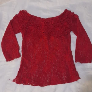 Röd spetsblus - Säljer en superfin röd spetsblus med trekvartsärm. Den har en romantisk offshoulder-design och är perfekt för festliga tillfällen. Blusen är i ett genomskinligt spetsmaterial som ger en elegant look. Perfekt för att piffa upp garderoben!,köpt i en secondhand butik,den har en skada vid naken som inte ens syns
