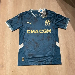 Marseille tröja  - Säljer en replika av Olympique Marseilles bortatröja 24/25, storlek S. Tröjan är i perfekt skick, aldrig använd och har alla originaltaggar kvar.