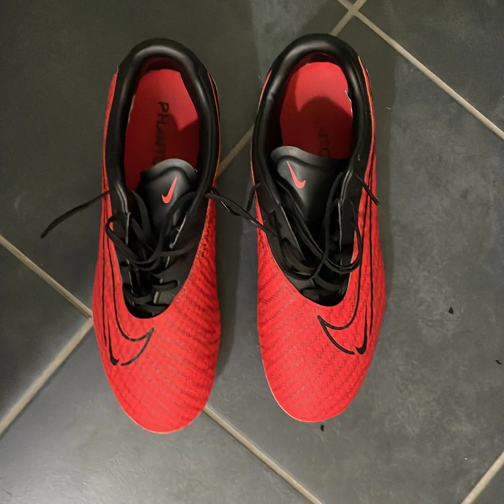 Säljer ett par snygga röda fotbollsskor från Nike i mycket bra skick. Skorna har en cool svart swoosh-design och snörning för perfekt passform. Perfekta för fotbollsträning eller match. Sulan har bra grepp för konstgräs eller gräsplaner.. Skor.