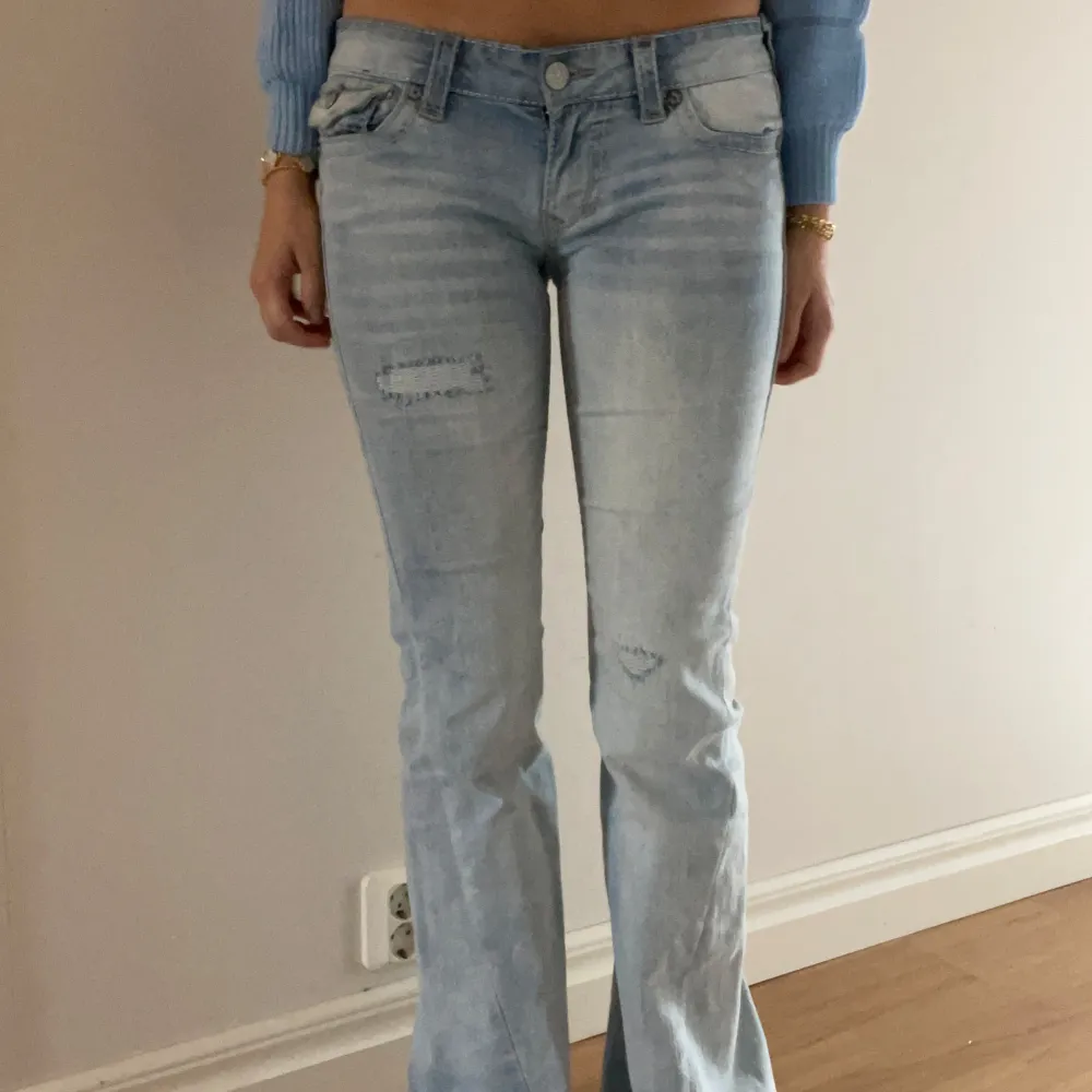 Säljer ett par ljusblå jeans från True Religion i bra skick. De har en snygg bootcut-stil och är dekorerade med slitningar på framsidan.. Jeans & Byxor.