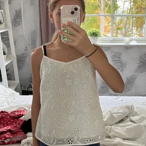 Vit blommig linne - Säljer en superfin vit linne med broderade blommor. Den har söta rosetter på axelbanden. Perfekt för sommardagar eller en avslappnad vårlook. Materialet är lätt och luftigt, vilket gör den bekväm att bära hela dagen.