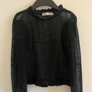 Svart spetsblus från Zara - Säljer en elegant svart spetsblus från Zara i storlek S. Blusen har långa ärmar och en fin volangdetalj vid halsen och ärmsluten. Perfekt för en festlig kväll eller en stilren vardagslook. 🖤