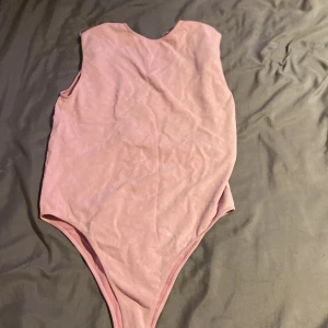 Rosa rygglös body från  Zara - Säljer en söt rosa bodysuit från Zara i storlek M-L. Den är ärmlös och har en enkel design som passar perfekt till både vardag och fest. Materialet är mjukt och stretchigt för en bekväm passform. Perfekt att matcha med jeans eller kjol för en stilren look!