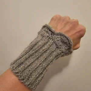 Grå stickade handledsvärmare - Säljer ett par grå stickade handledsvärmare. De är ribbstickade och har en söt rosett-detalj upptill. Perfekta för att hålla handlederna varma under kyliga dagar. Passar bra till både vardag och lite finare tillfällen. Supermysiga och stilrena!