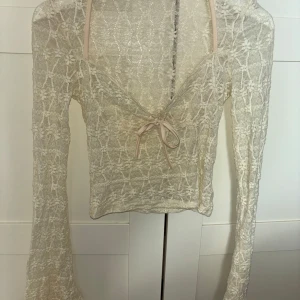 Vit spetsblus med knytning - Långärmad vit spetsopp med en knytning framtill och lite utsvängda armar. Så så fin och går lätt att styla med vilken underdel som helst🩷 Storlek S/M från Venderbys