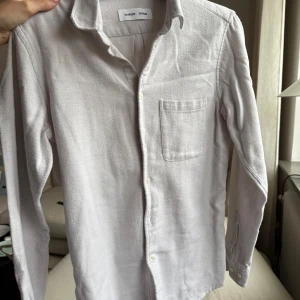 Ljus skjorta från Samsøe Samsøe - Säljer en ljusgrå skjorta från Samsøe Samsøe i mycket bra skick pga för liten för mig. Skjortan har en klassisk design med långärmade ärmar och en bröstficka. Materialet känns mjukt och bekvämt mot huden. Mycket bra skick!