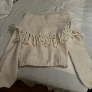 Vit stickad tröja med fransar - Superfin vit stickad tröja med fransdetaljer över bröstet. Perfekt för att hålla sig varm och snygg under kyliga dagar. Tröjan har en lös passform och långa ärmar, vilket gör den både bekväm och stilren. Passar perfekt till både vardag och fest!