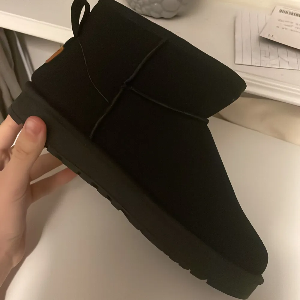 Säljer ett par svarta boots i syntetmaterial med en cool etikett där det står 'Sport Best Fashion'. De har en robust sula med bra grepp och en enkel design utan snörning. Perfekta för höst och vinter när du vill hålla fötterna varma och stiliga. UGG kopior och säljs till mycket bättre pris. Storlek tror jag är 40-42. Kengät.