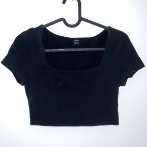Svart croppad topp - Snygg svart croppad topp i bomull. Perfekt för sommardagar eller en utekväll. Den har en enkel design med korta ärmar och en rund halsringning. Passar bra till både jeans och kjol!