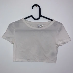 Vit croppad t-shirt - Säljer en enkel och stilren vit croppad t-shirt. Perfekt för sommardagar eller som ett basplagg i garderoben. T-shirten har korta ärmar och en rund halsringning. Passar till både jeans och kjol för en avslappnad look.