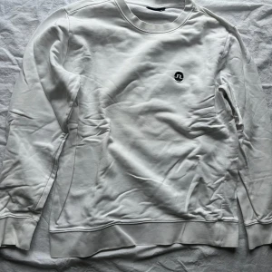 Vit tröja från J.Lindeberg - Säljer en stilren vit tröja från J.Lindeberg i storlek L. Tröjan har en broderad logga på bröstet och är i mycket bra skick. Bra för både vardag och fest. Den är långärmad och gjord i ett mjukt material som känns skönt mot huden.