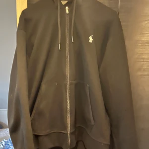 Svart hoodie från Ralph Lauren - Säljer en klassisk svart hoodie från Ralph Lauren med dragkedja och huva. Den har en liten broderad logga på bröstet och är i mycket bra skick. Perfekt för höst och vinter, och passar till både vardag och träning.