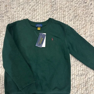 Grön tröja från Polo Ralph Lauren - Säljer en snygg grön tröja från Polo Ralph Lauren i nytt skick. Den har en klassisk design med långärmade ärmar och en liten röd logga på bröstet. Perfekt för höst och vinter, och den är supermjuk på insidan. Passar både till vardags och lite finare tillfällen. 🌿