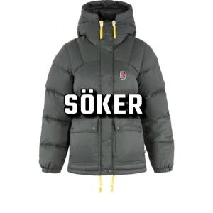 söker grå fjällräven jacka - Söker en grön pufferjacka från Fjällräven med huva och gula detaljer. Jackan har en dragkedja och knappar framtill samt långa ärmar. Perfekt för kalla dagar med sin varma och vadderade design.