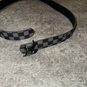 Rutig bälte med svart spänne - Säljer ett stilrent bälte med svart och grått rutmönster. Bältet har ett elegant svart spänne som ger en lyxig känsla. Perfekt för både vardag och festliga tillfällen. Passar bra till jeans eller kostymbyxor. (SKICKA DITT PRIS PRV)