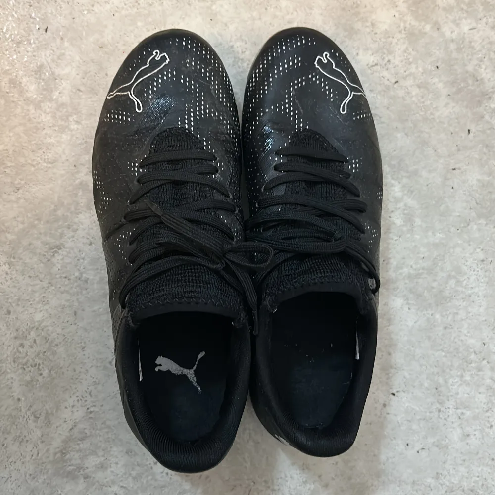 Säljer ett par svarta fotbollsskor från Puma i bra skick. Skorna har en snygg design med vita detaljer och snörning. Perfekta för fotbollsträning eller match. Sulan har dobbar för bra grepp på planen. Skorna är bekväma och ger bra stöd för fötterna.. Kengät.