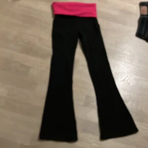 Svarta byxor med rosa midja - Säljer ett par svarta byxor med en bred, rosa midja .. Midjan har glittriga bokstäver som stavar 'PINK'. Byxorna är i bootcut-stil och passar perfekt för en avslappnad look. Superbekväma och stiliga!