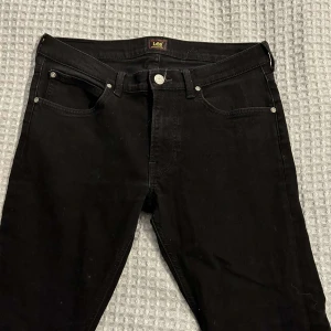 Svarta jeans från Lee storlek W31 L30 - Säljer ett par svarta jeans från Lee i mycket bra skick. De har en klassisk femficksdesign med knapp och dragkedja framtill. Perfekta för både vardag och fest! 🖤