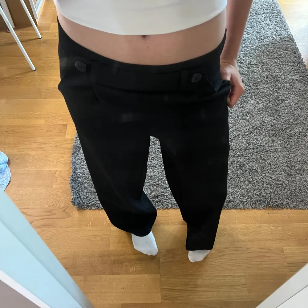 Säljer ett par svarta kostymbyxor som är midwaist men går att använda sol lowwaist och har snygga knappar framtill. De är i en loose passform och ser riktigt bekväma ut. Perfekta för både vardag och fest!. Jeans & Byxor.