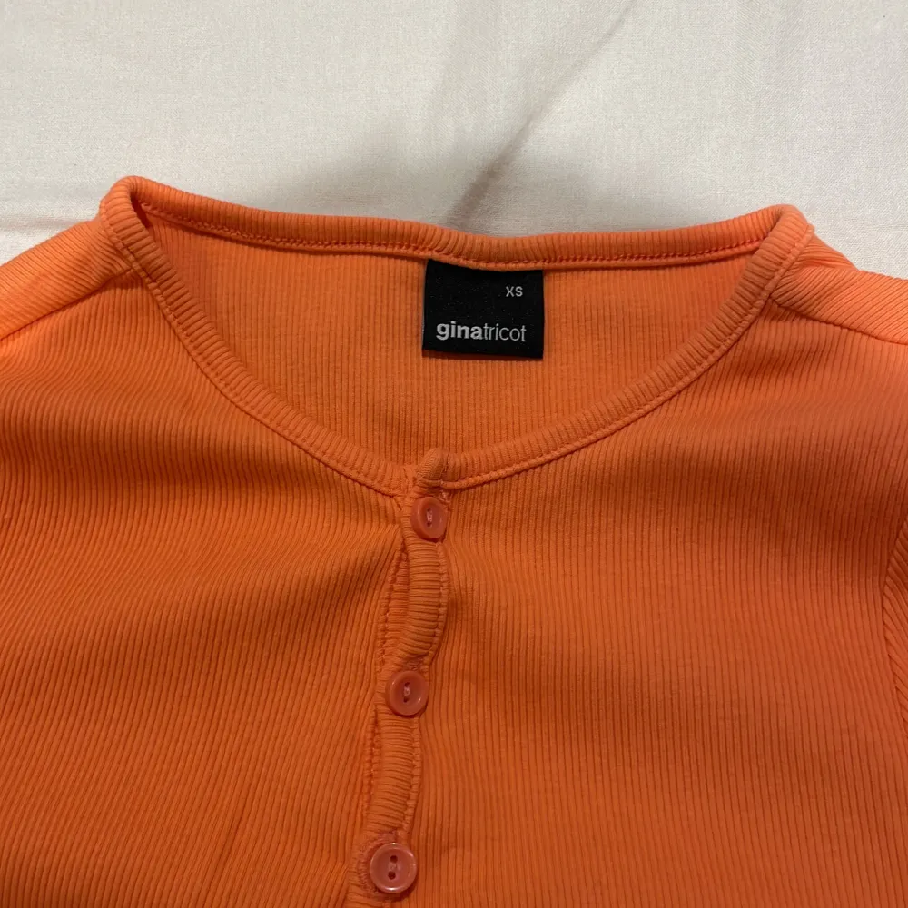 Säljer en superfin orange ribbad topp från Gina Tricot i storlek XS. Den har korta ärmar och knappar framtill som ger en snygg detalj. Perfekt för sommardagar eller som en färgglad bas i garderoben!. Toppar.