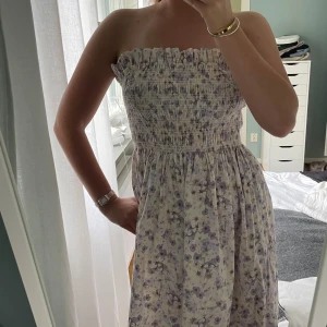 Blommig axelbandslös klänning - Säljer en superfin axelbandslös klänning med blommigt mönster från Hm❣️. Den har en smockad överdel och ett luftigt fall. Perfekt för sommar, fest eller att ha under en stickad tröja🥰