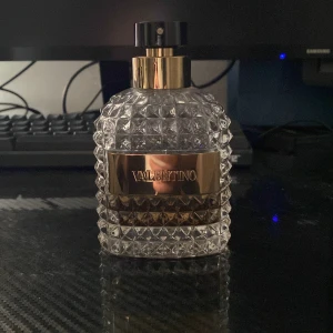 Valentino parfymflaska - Säljer en snygg parfymflaska från Valentino. Flaskan är genomskinlig med ett coolt mönster av små pyramider. Den har en svart spraytopp och luktar riktigt lyxigt! 100ml flaska men innehåller 40ml kvar