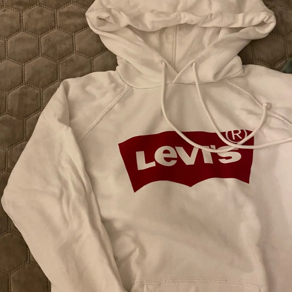 Säljer en snygg vit hoodie från Levi's i storlek S. Den har en klassisk röd Levi's-logga på bröstet och är perfekt för en casual look. Hoodien är i mjukt material och har en bekväm passform med dragsko i huvan.. Hoodies.