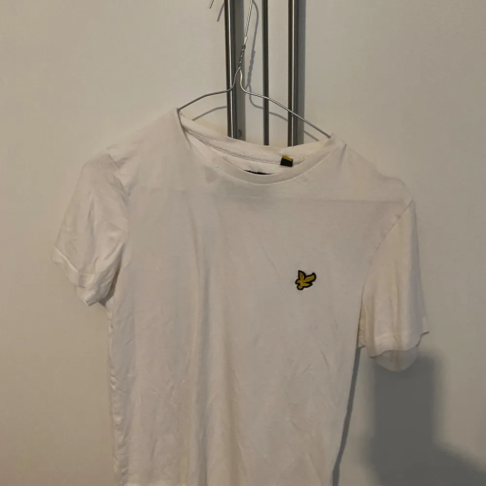 Säljer en klassisk vit t-shirt från Lyle & Scott. Den har en liten gul logga på bröstet och är i bomull. Perfekt för en avslappnad stil eller som basplagg i garderoben. Kortärmad och i bra skick!. T-shirts.