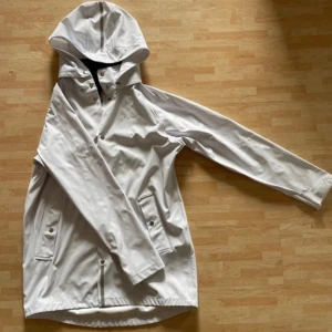 Regnkappa från Everest  - En vit/ljuslila regnkappa från Everest i storlek 164. Luvan går att ta bort och sitter fast med samma knappar som man  stänger med. Den är lite smutsig på ett ställe som visas på sista bilden. Annars i fint skick.