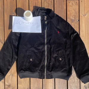 Svart manchesterjacka från Polo Ralph Lauren - Helt ny svart manchesterjacka i klassisk Baracuda-stil från Polo Ralph Lauren, tillgänglig i storlekarna Small. Jackan är tillverkad i högkvalitativ bomull, med den karakteristiska manchesterstrukturen. Perfekt för både vardagsbruk. 