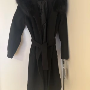 äkta hollies kappa CAMILLA  - Äkta hollies kappa i modellen CAMILLA. Storlek 34. Finns fickor, luva och pälsen går att ta av. Köpt i Johnells ett par månader sen och har aldrig använts, etikett finns kvar på kappan. Skriv vid intresse!!!